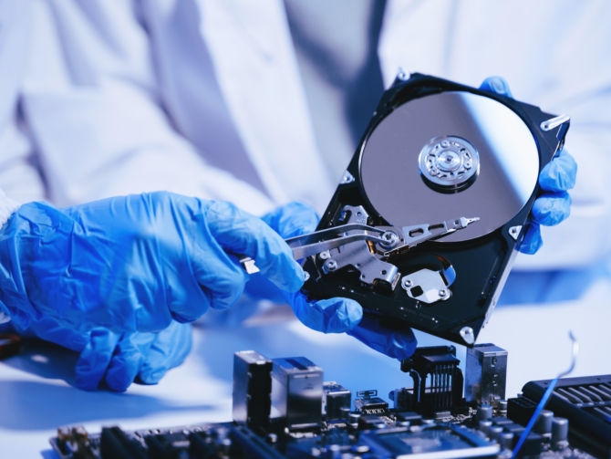 Mavi statik eldiven giyen teknisyen, elinde açık sabit disk tutarak veri kurtarma işlemi yapıyor